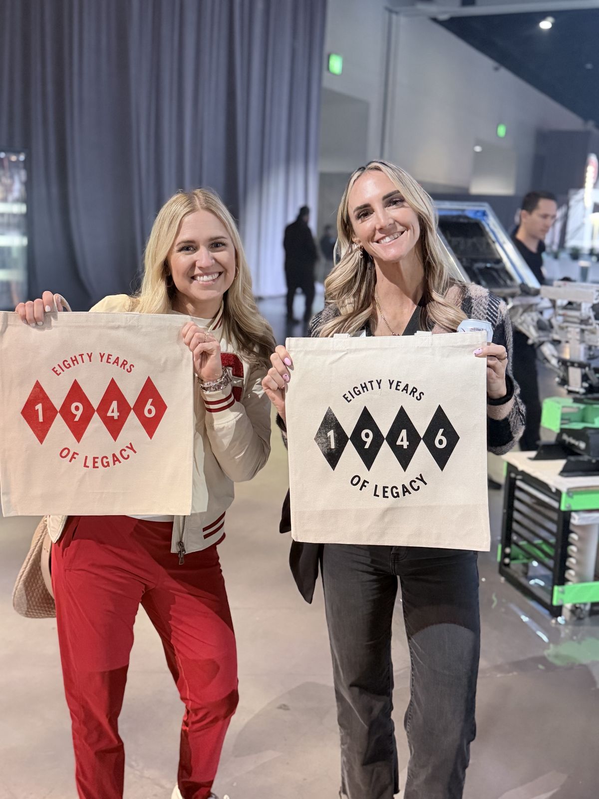 Two guests holding matching personalized anniversary tote bags at a corporate showcase